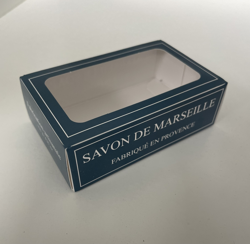 Eine dunkelgrüne, rechteckige Seifendose von Dampa 1975 mit transparentem Sichtfenster und weißem Text "Savon de Marseille Fabriqué en Provence" deutet auf Marseiller Seife mit Bio-Olivenöl-Limettenduft hin. Die leere Dose ruht auf einer weißen Fläche.