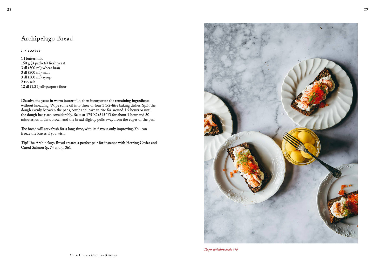 Eine Seite aus „Es war einmal eine Landhausküche“ von Cozy Publishing zeigt drei belegte Brötchen mit cremigem Aufstrich, geräuchertem Lachs und Rogen neben einer Schale mit Zitronen auf weißem Marmor und hebt die reinen Zutaten hervor.