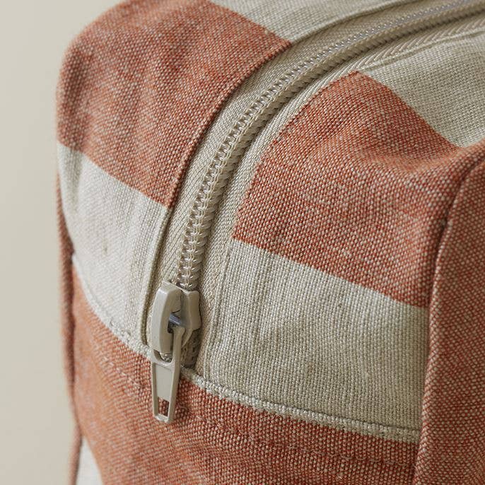 Nahaufnahme des Sylvie Thiriez | Kulturtbeutel Mistral ziegelrot klein, mit dicht gewebtem, strukturiertem Stoff mit kräftigen rostorangen und gebrochen weißen Streifen, Metallreißverschluss und OEKO-TEX® STANDARD 100 zertifizierter Qualität.