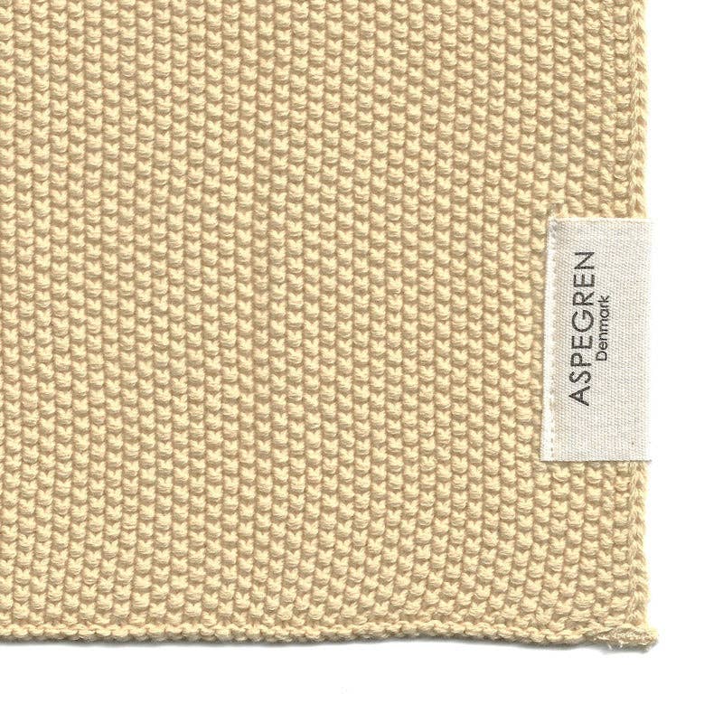 Goldfarbenes, gestricktes Geschirrtuch aus umweltfreundlicher Bio-Baumwolle von Aspegren Denmark mit weißem Randetikett und schwarzem Text "ASPEGREN Denmark".