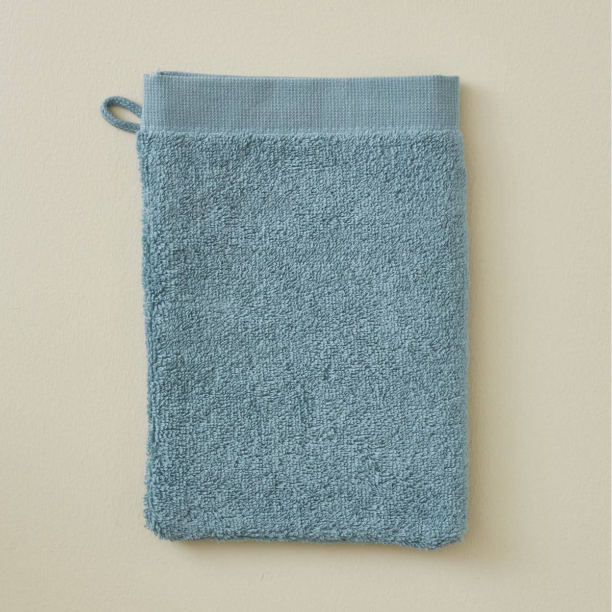 Der Sylvie Thiriez Waschlappen aus Frottee in Blau mit einer Stoffschlaufe liegt flach auf einer hellbeigen Fläche.