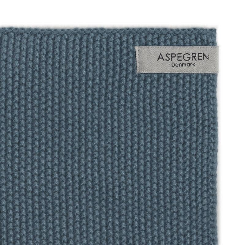 Eine Nahaufnahme der Spültücher „Aspegren Denmark – Gestrickt – Einfarbig – Blau“ zeigt ihren strukturierten blauen Strick aus umweltfreundlicher Baumwolle mit einem beigefarbenen Etikett mit der Marke „Aspegren Denmark“ in der oberen rechten Ecke.