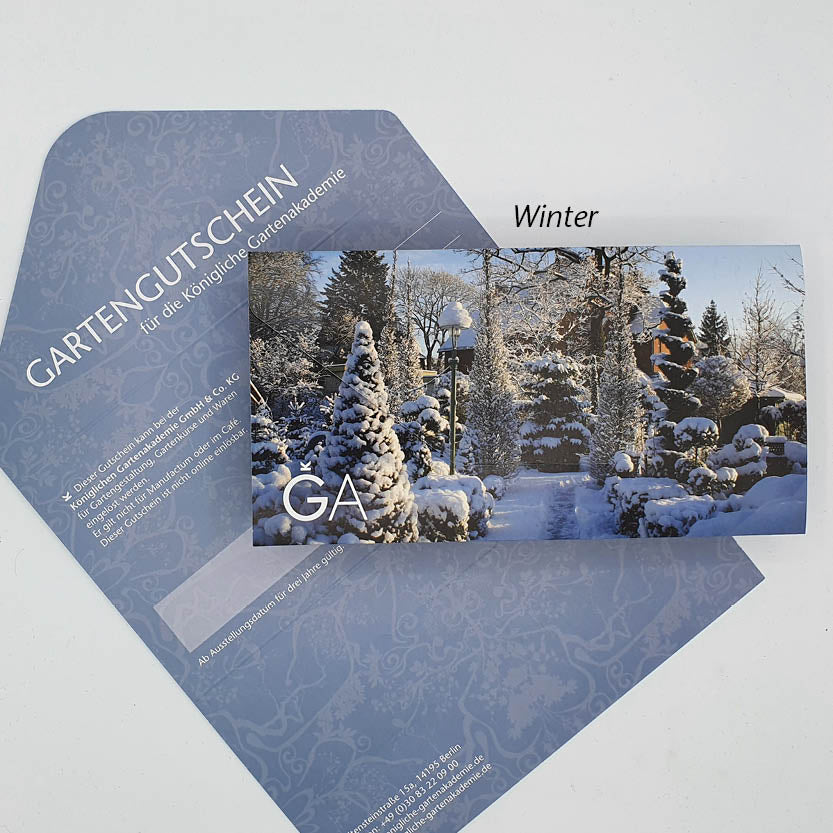 Der Gutschein für die Königliche Gartenakademie von Königliche Gartenakademie zeigt winterliche Motive mit verschneiten Bäumen und Laterne auf einem blauen Umschlag – das perfekte Geschenk für Gartenliebhaber.