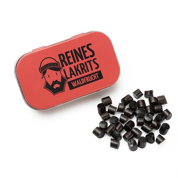 Eine geöffnete rote Dose LASSE LAKRITS - natürlich lecker - Dose Reines Lakritz Waldfrucht, auf der ein bärtiges Gesicht abgebildet ist, steht neben verstreuten zuckerfreien Lakritz Waldfrucht Bonbons.