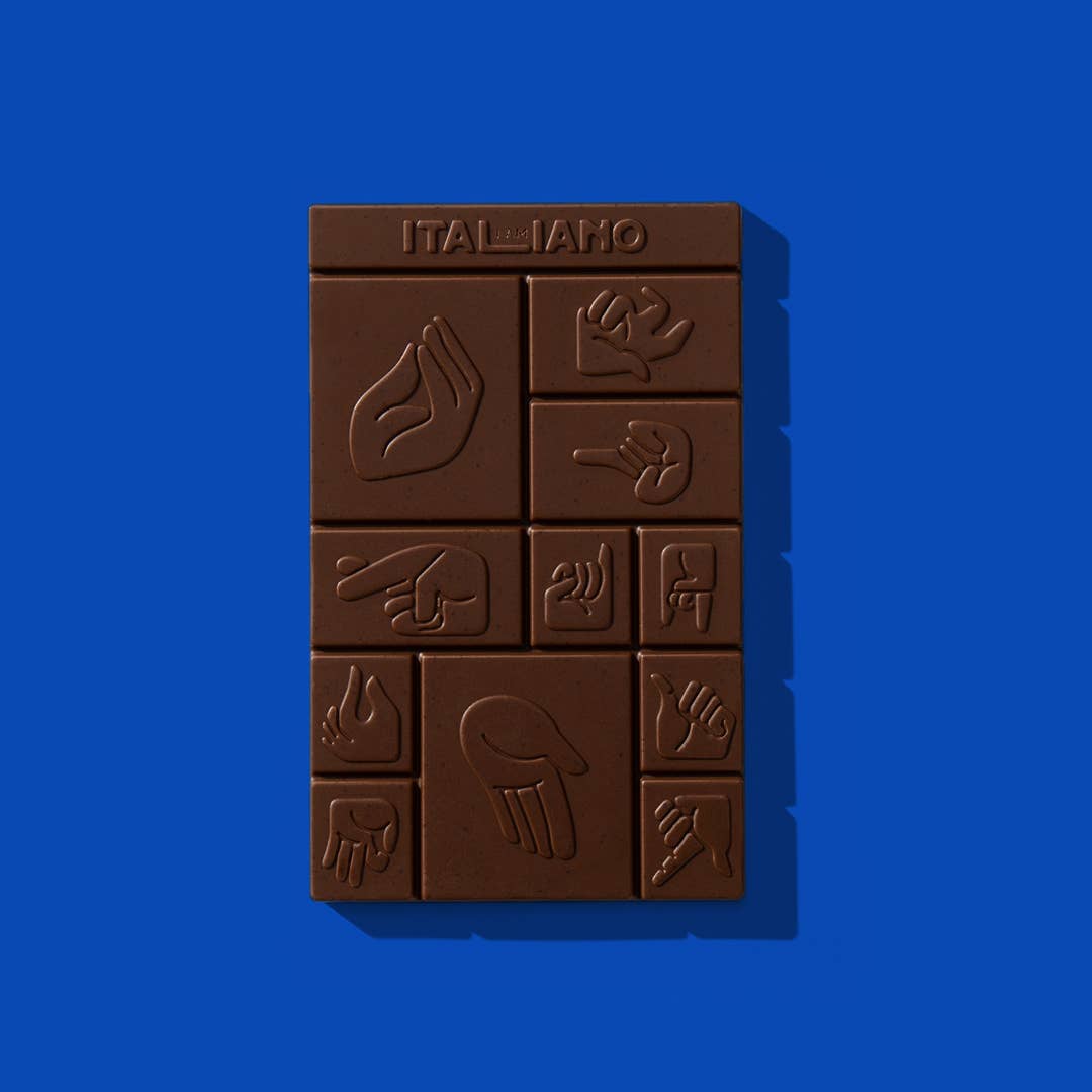 Eine Tafel I AM ITALIANO - Rom Bio-Schokolade mit Karamell und Salz mit geprägten Handzeichen in einem Raster steht auf einem hellblauen Hintergrund. Das I AM ITALIANO-Logo erscheint oben auf der Schokolade.