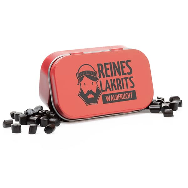 Eine rote, rechteckige LASSE LAKRITS-Dose mit der Aufschrift "Reines Lakritz Waldfrucht" und der Abbildung eines bärtigen Gesichts, umgeben von verstreuten Stücken zuckerfreier schwarzer Lakritze.