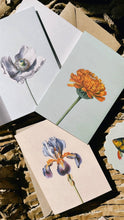 Lade das Bild in den Galerie-Viewer, Die 30x40 - Anemone Leporello Grußkarte von 30x40 zeigt botanische Illustrationen auf Recyclingpapier, darunter eine weiße Blume, eine orange Blume und eine violette Iris; gedruckt in Deutschland.
