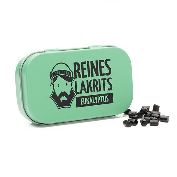 Eine grüne LASSE LAKRITS-Dose mit der Aufschrift "Reines Lakrits Eukalyptus" und der Abbildung eines bärtigen Mannes steht neben mehreren Stücken zuckerfreier Lakritz-Bonbons.