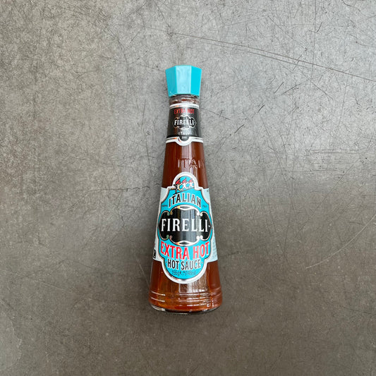 A 148ml Glasflasche Firelli - Casa Firelli Extra scharfe italienische Sauce von Firelli mit blauem Deckel und Etikett steht aufrecht auf einer strukturierten grauen Oberfläche.