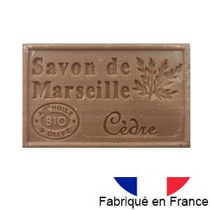 Ein braunes Stück Dampa 1975 - Marseiller Seife mit Bio-Olivenöl-Zedern weist einen Zedernduft, eine Olivenzweigillustration, einen Bio-Olivenöl-Stempel und ein kleines französisches Flaggensymbol mit der Aufschrift „Fabriqué en France“ darunter auf.