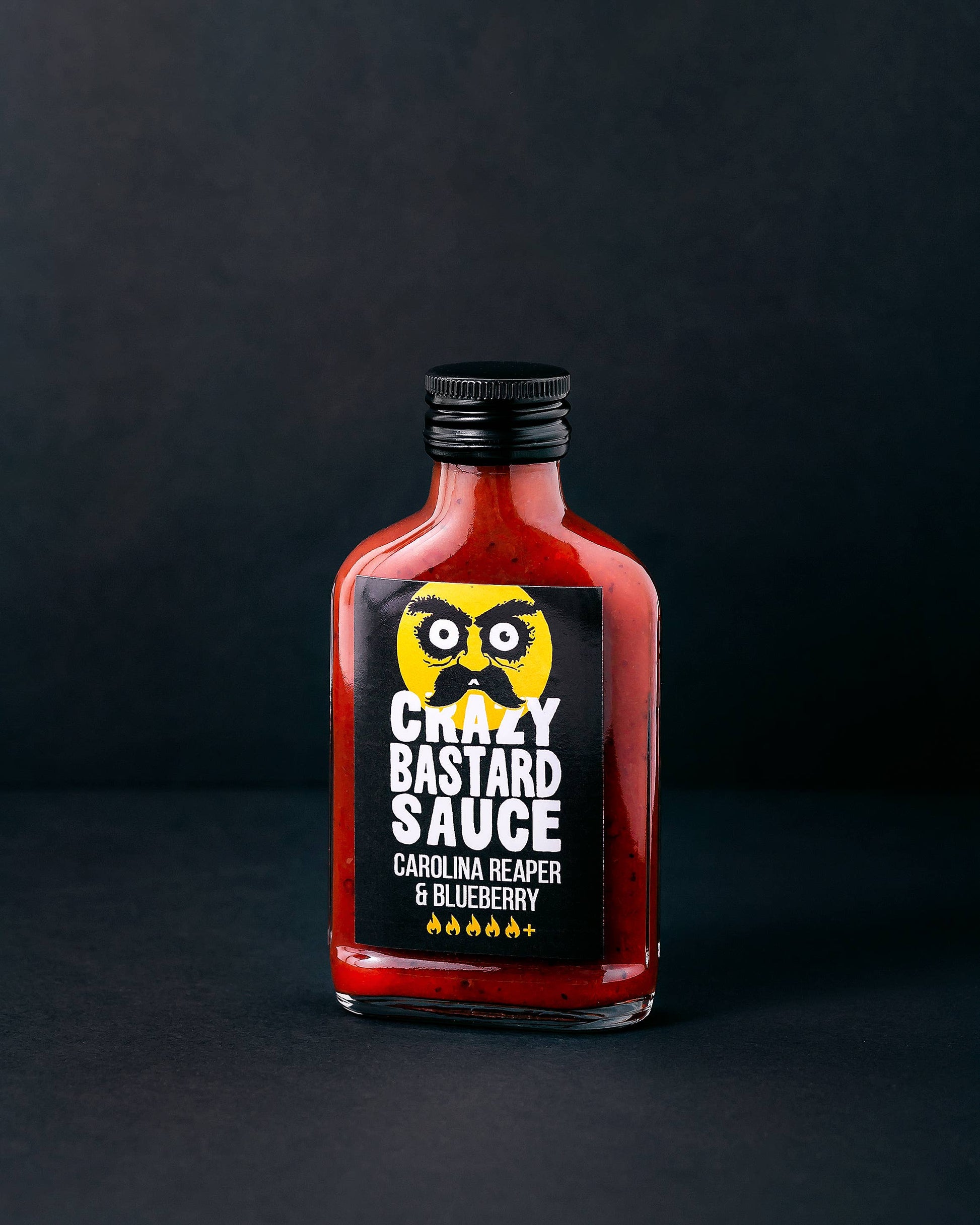 Die 100-ml-Flasche der CBS Foods GmbH (Crazy Bastard Sauce) - Carolina Reaper & Blueberry hat ein schwarzes Etikett mit einer gelben Eule, fünf Chili-Symbolen für hohe Schärfe und einem dunklen Hintergrund.