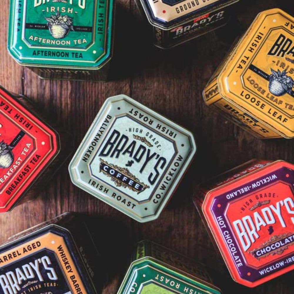 Verschiedene Dosen der Brady's Coffee Company, darunter auch Bradys Loose Leaf Tea, werden auf einer Holzoberfläche präsentiert und heben eine lebendige Auswahl an irischem Tee, Kaffee und heißer Schokolade hervor.