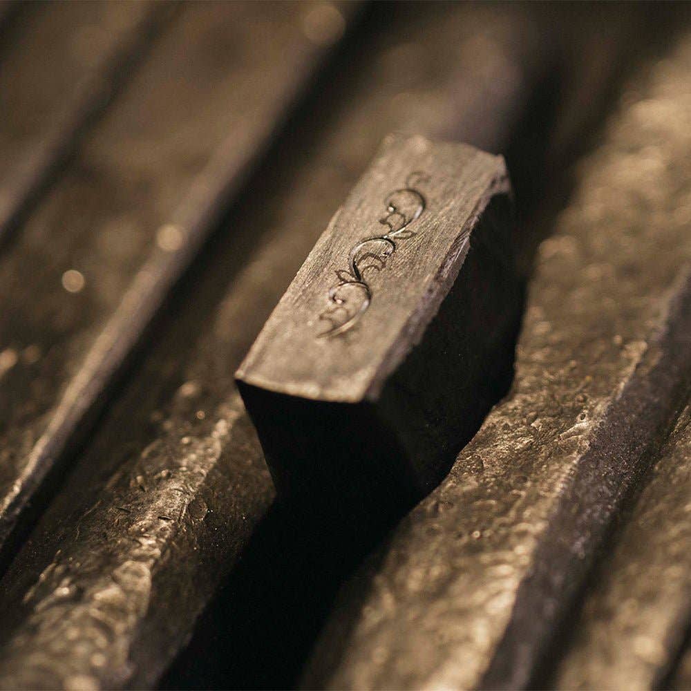 Eine Nahaufnahme des ENTREPÔT - YSTUDIO Klassische Renaissance KAZARI KANAGU ORCHID Tintenroller, ein dunkler Metallstift mit dekorativen Metallgravuren, der auf strukturierten Metallstäben ruht.