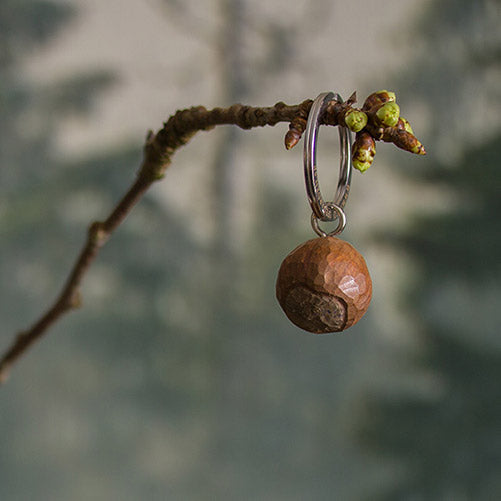 Der Wildlife Garden Handgefertigter Schlüsselanhänger aus Holz | Haselnuss baumelt an einem Zweig vor unscharfem Wald - ein ideales Geschenk für Naturfreunde.