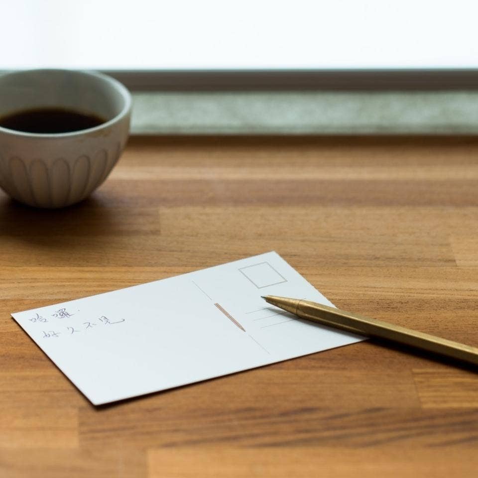 Der ENTREPÔT - YSTUDIO Klassischer Revolve Kugelschreiber Feder aus Messing liegt stilvoll auf einer Postkarte mit japanischer Schrift, bereit für langlebige Notizen-ästhetisch und hochwertig von ENTREPÔT.