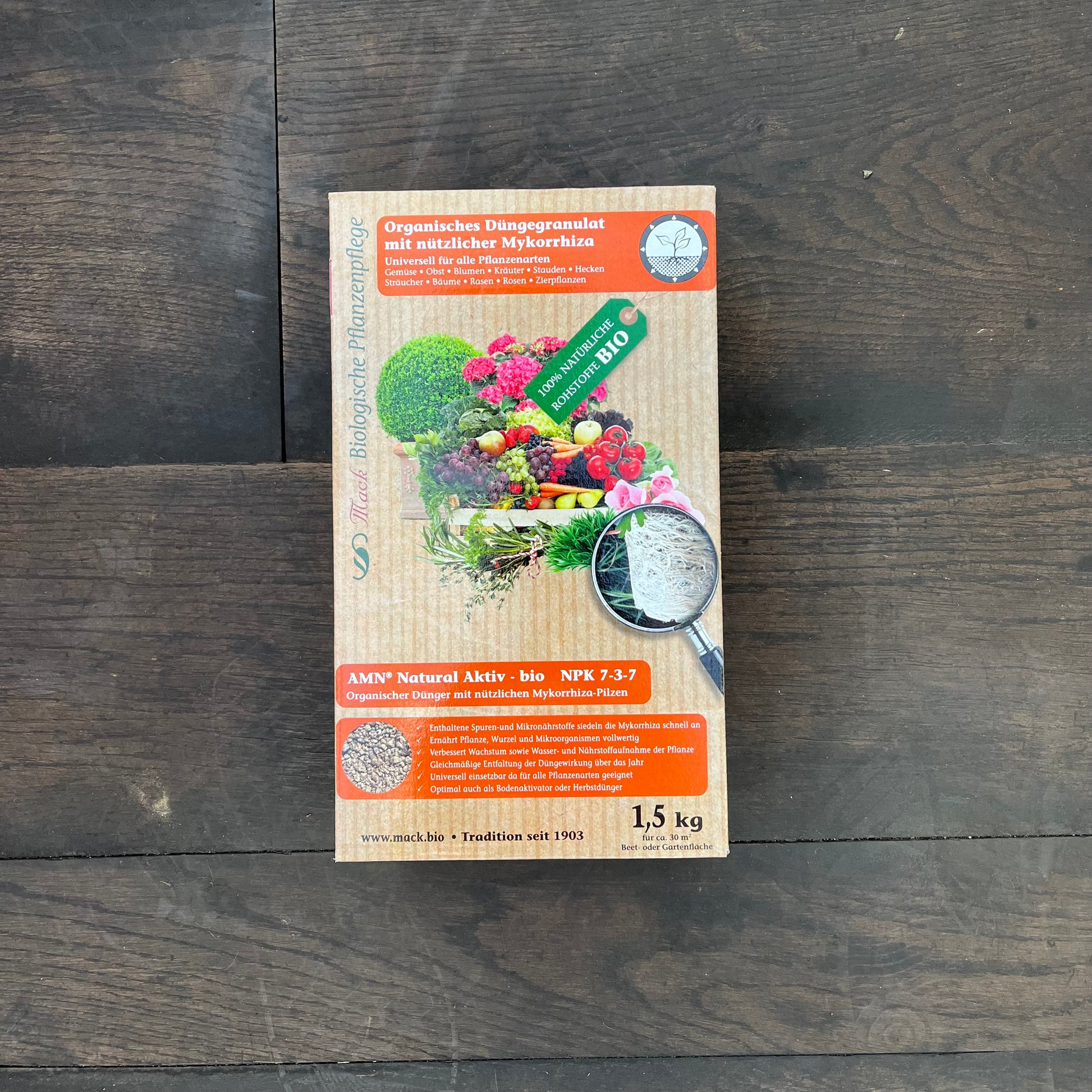 Auf einem dunklen Holzboden steht eine 1,5 kg schwere Schachtel mit dem organischen Dünger AMN Natural Aktiv-bio von AMN, der natürliche Mykorrhiza enthält und auf dessen Etikett Bilder von Gemüse und Gartenprodukten zu sehen sind.