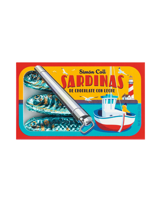 Eine bunte Schachtel mit der Aufschrift "Simón Coll | Schokosardinen aus Vollmilchschokolade" von Simon Coll enthält drei in Folie verpackte Sardinen aus Vollmilchschokolade und einen Dosenöffner aus Metall mit Abbildungen von Fischerbooten und Leuchttürmen.