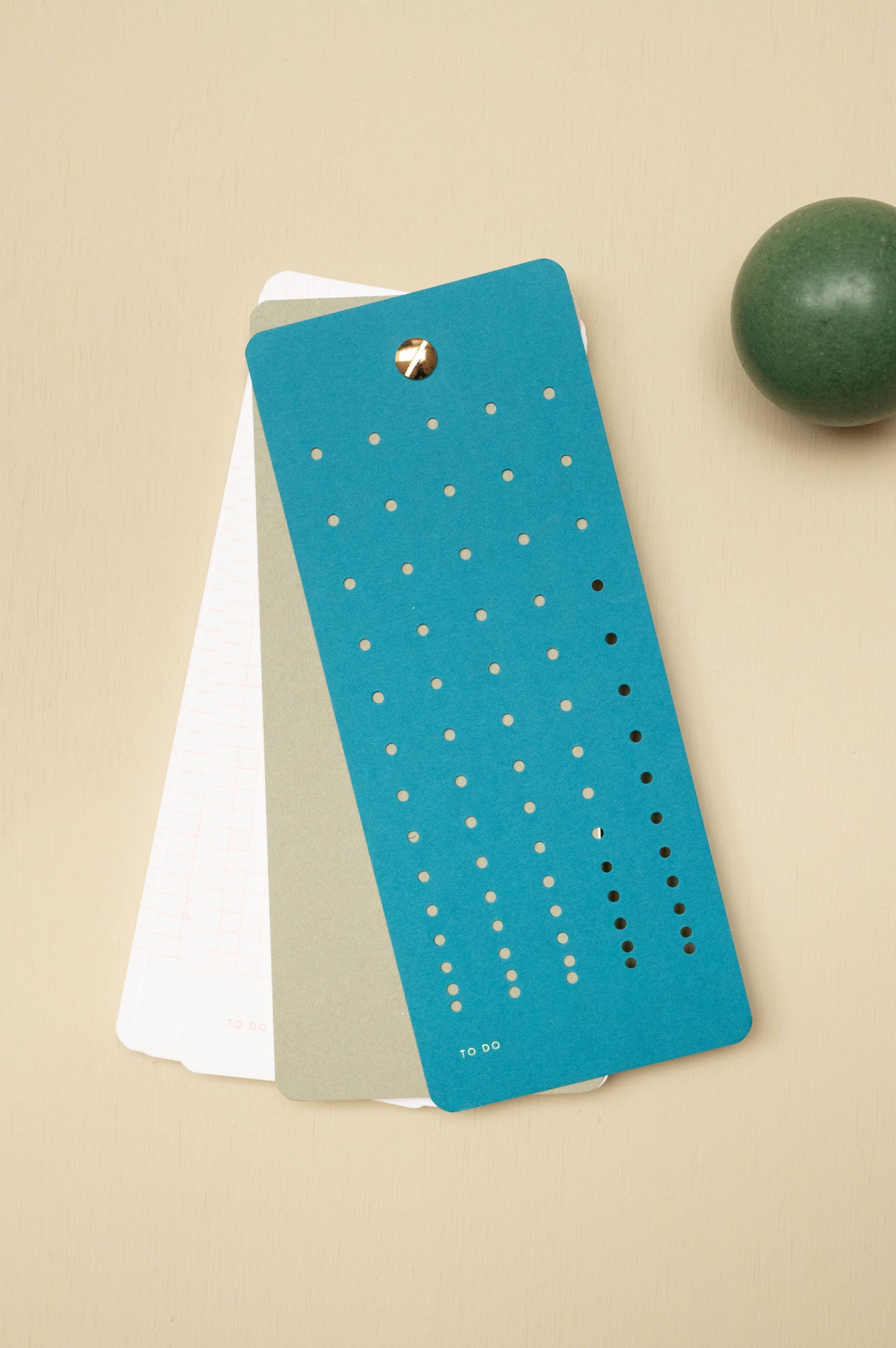 Die Tinne Mia - Aufgabenliste - Blaugrün von Tinne Mia ist ein Set aus FSC®-zertifizierten, rechteckigen Karten mit einer blau-grünen Oberkarte mit Lochreihen und dem Schriftzug TO DO" am unteren Rand, die durch einen Messingverschluss zusammengehalten werden.