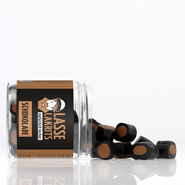 Eine durchsichtige LASSE LAKRITS - natürlich lecker - Dose Lakritz Schokolade liegt auf der Seite und verschüttet runde schwarze Bonbons mit braunem Kern auf eine weiße Fläche.