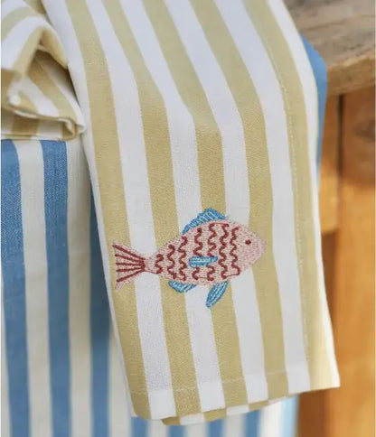 Die Sylvie Thiriez - Serviette von Sylvie Thiriez verfügt über blaue, weiße und braune Streifen, Eleganz und Qualität sowie einen bestickten rosa Fisch mit blauen Flossen und Schwanz. Die hochwertigen Stoffe werden auf einer Holzoberfläche präsentiert.