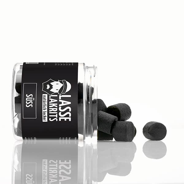 Ein LASSE LAKRITS - natürlich lecker - Dose Lakritz Süss Glas mit schwarzer und weißer Grafik liegt auf der Seite und verschüttet süße Lakritzbonbons auf eine weiße Oberfläche. Auf dem Etikett stehen "natürlich lecker" und "süß".