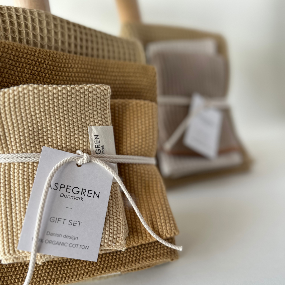 Nahaufnahme des beigefarbenen Aspegren Denmark - Geschenkset - Melone Spültücher aus Bio-Baumwolle, ordentlich gefaltet und mit weißer Schnur gebunden - eine perfekte Geschenkidee für die Küche von Aspegren Denmark, mit weiteren Sets im Hintergrund.