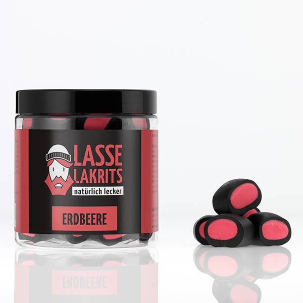 Ein durchsichtiges Glas mit der Aufschrift LASSE LAKRITS - natürlich lecker - Dose Lakritz Erdbeere enthält schwarze und rosa Lakritzbonbons von LASSE LAKRITS. Auch außerhalb des Glases sind auf einer weißen Fläche mehrere Lakritz Erdbeere-Bonbons abgebildet.