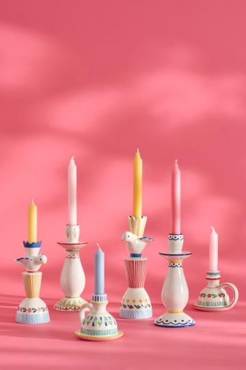Sechs handbemalte IB Laursen Kerzenhalter aus Keramik in weiß und blau gemustert sind auf einer rosa Fläche arrangiert und zeigen verspielte Designs vor pinkem Hintergrund.