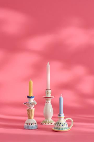 Drei lebendige IB Laursen Kerzenhalter aus Keramik - zwei in weiß / blau gemustert und einer in rosa - zeigen pastellfarbene Kerzen (gelb, rosa, blau) mit dekorativen Mustern auf einem rosa Hintergrund und weichen Schatten.