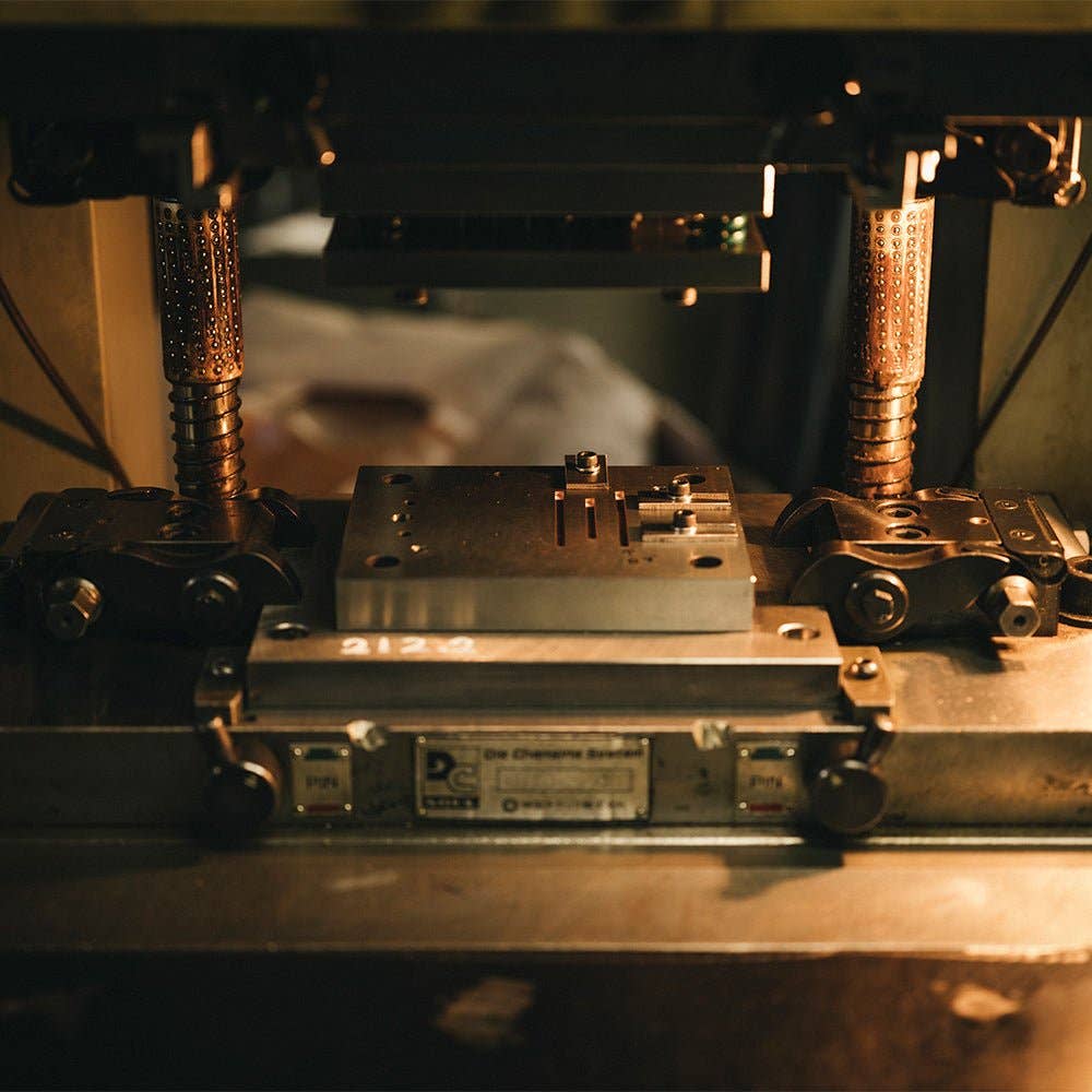 Nahaufnahme des ENTREPÔT YSTUDIO Klassische Renaissance KAZARI KANAGU ORCHID Tintenrollers, der von Kazari Kanagu inspirierte Metallarbeiten und mechanische Details in einer warm beleuchteten Werkstattumgebung zeigt.