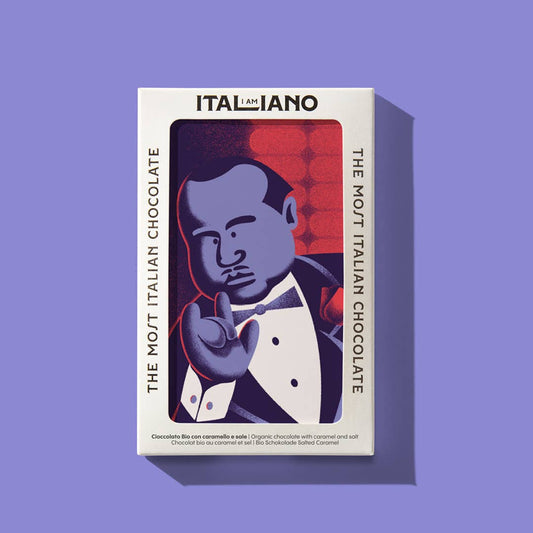 Eine Schachtel I AM ITALIANO - Padrino Bio-Schokolade mit Karamell und Salz, auf der ein Mann im Smoking eine italienische Handbewegung macht, steht vor einem hellvioletten Hintergrund und hebt die ITALIENISCHSTE SCHOKOLADE hervor.