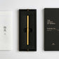Ein goldener ENTREPÔT - YSTUDIO Klassischer Revolve-Rollerball-Stift (Messing) mit stabilem Griff liegt in einer schwarzen Schachtel zwischen einem weißen japanischen Heft und einem schwarzen Deckel mit der Aufschrift THE WEIGHT OF WORDS. Auf beiden Deckeln ist die Marke ENTREPÔT zu sehen.