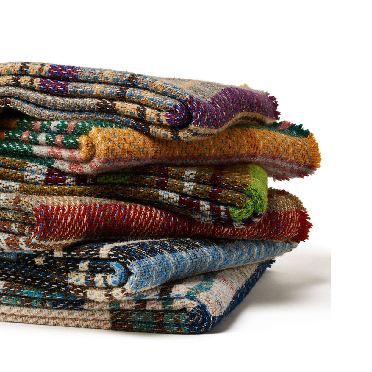 Eine Auswahl an farbenfrohen Tweedmill | Zufällige recycelte Wolldecke - Groß - verschiedene Farben von Tweedmill Textiles mit traditionellen Mustern ist kunstvoll vor weißem Hintergrund gestapelt.