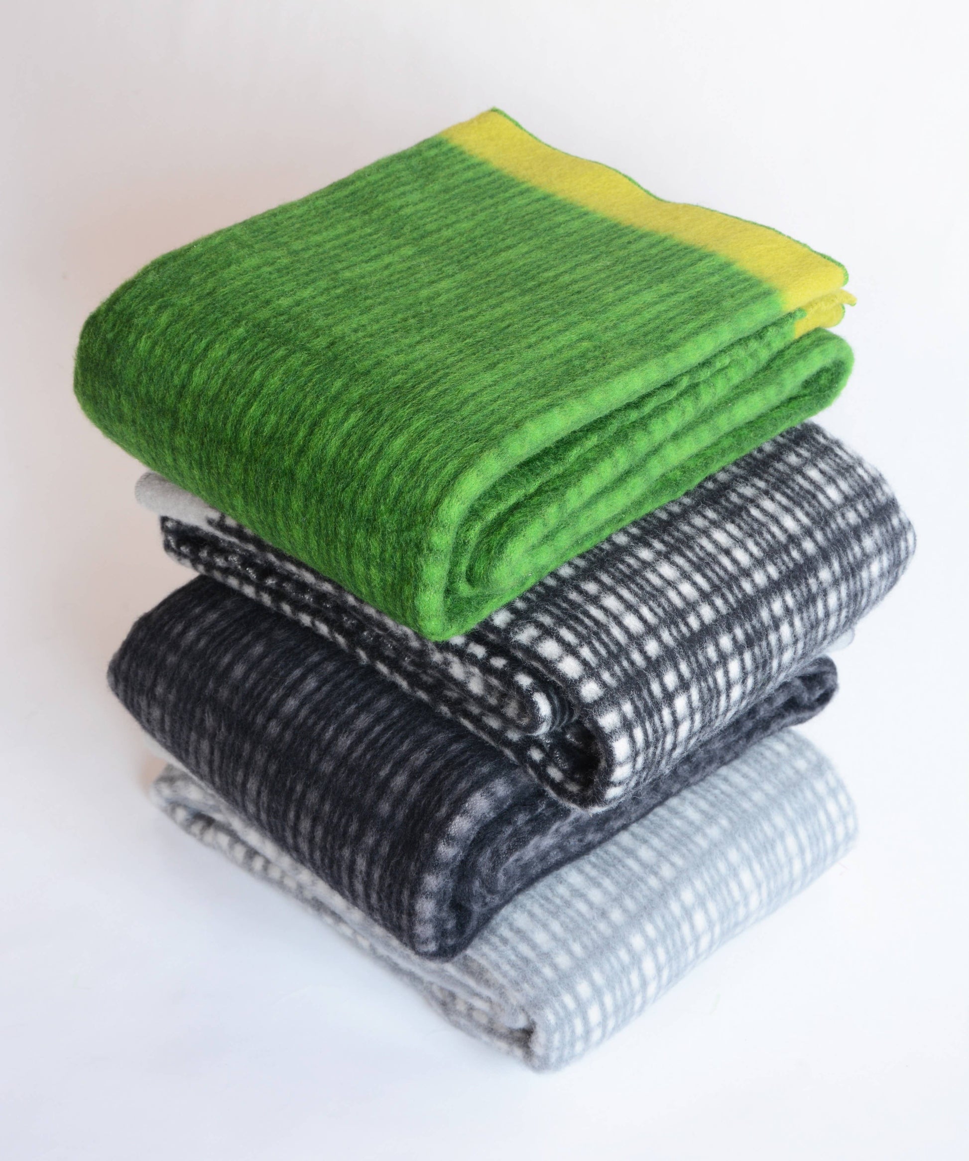 Ein Stapel von drei Sofie Sjöström Design-Decken, darunter die grüne "Darling Tagesdecke aus Lammwolle | Kiwi" obenauf, alle aus neuseeländischer Lammwolle, ordentlich gefaltet auf weißem Grund.