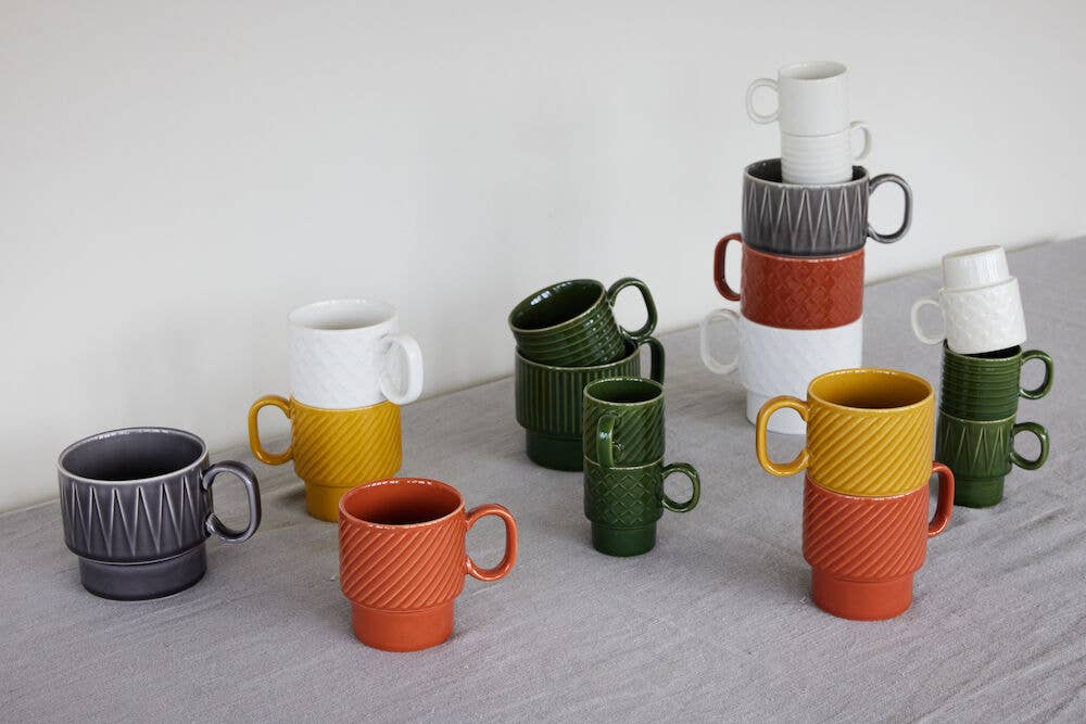 Bunte Sagaform GmbH Coffee & More Teetasse, 2-tlg. Keramikbecher mit strukturierten Mustern sind auf einer grauen Stoffoberfläche vor einem schlichten weißen Hintergrund gestapelt und gruppiert.