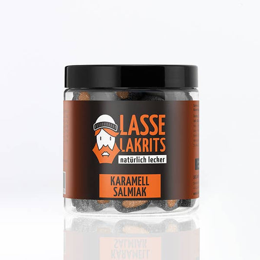 Ein durchsichtiges LASSE LAKRITS-Glas mit schwarzem Deckel enthält Dose Karamell Salmiak-Bonbons. Das braune Etikett zeigt ein illustriertes bärtiges Gesicht mit weißer deutscher Schrift, alles vor einem schlichten weißen Hintergrund.