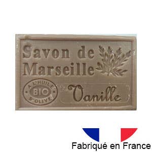 Ein beiges Stück Dampa 1975 Marseiller Seife mit Bio-Olivenöl-Vanille-Duft, zeigt ein Olivenzweig-Design, das Etikett „Savon de Marseille“ und eine kleine französische Flagge mit „Fabriqué en France“ unten rechts.