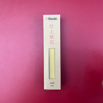 Der Niwaki-Schleifstein von Niwaki wird in einer braunen Schachtel mit roten japanischen Schriftzeichen und der Aufschrift „#3000 Fine“ auf einer roten Oberfläche geliefert – perfekt zum Schärfen von Klingen.
