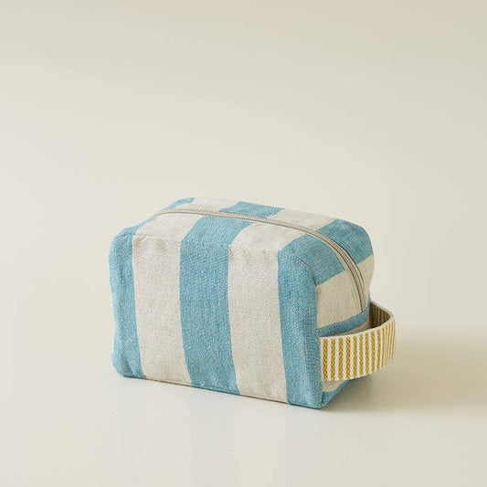 Der kleine Kulturbeutel "Mistral Türkis" von Sylvie Thiriez mit blauen und weißen Streifen, Reißverschluss und gelb-weiß gestreiftem Griff liegt auf einer hellen Oberfläche.