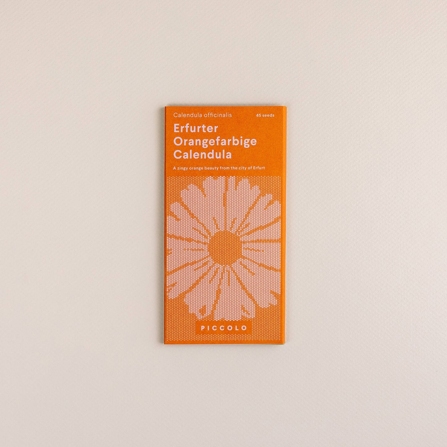 Ein Päckchen Piccolo Seeds | Ringelblume Erfurter Orangefarbene von Piccolo Seeds, mit einem orange-weißen Design mit einer stilisierten Blumenillustration, ist auf einem hellbeigen Hintergrund platziert.