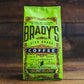Eine leuchtend grüne 227-g-Tüte Brady's Coffee Company - Brady's Celtic Blend Kaffee mit kunstvollen schwarz-goldenen Details liegt auf einer Holzoberfläche. Dieser gemahlene Kaffee von Brady's Coffee Company bietet Spezialitätenqualität.