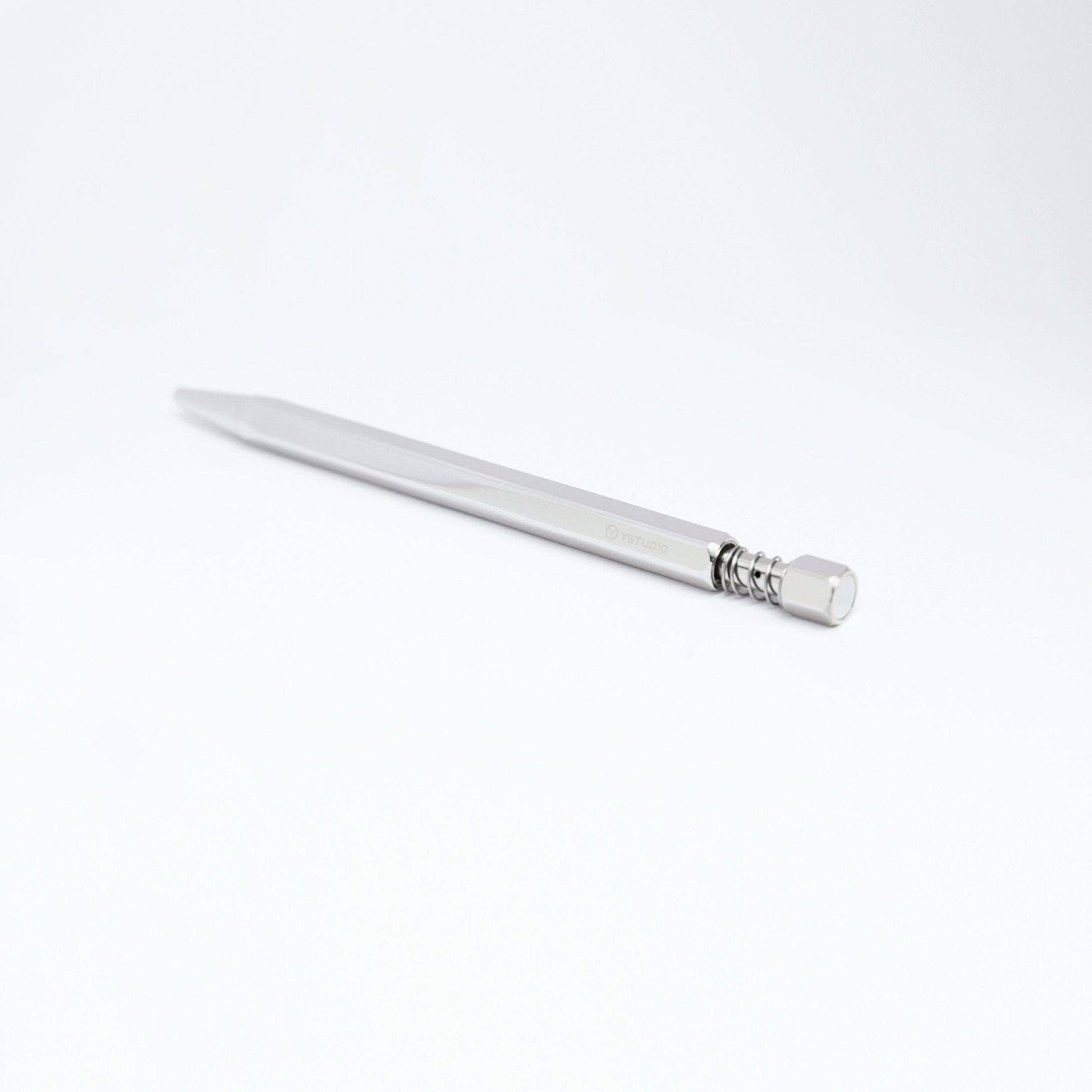 Eine schlichte, minimalistische ENTREPÔT - YSTUDIO Klassischer Drehkugelschreiber Feder (Glänzendes Silber) ruht diagonal auf einer weißen Fläche, mit dem Radiergummiende näher an der Kamera, und zeigt metallische Eleganz.