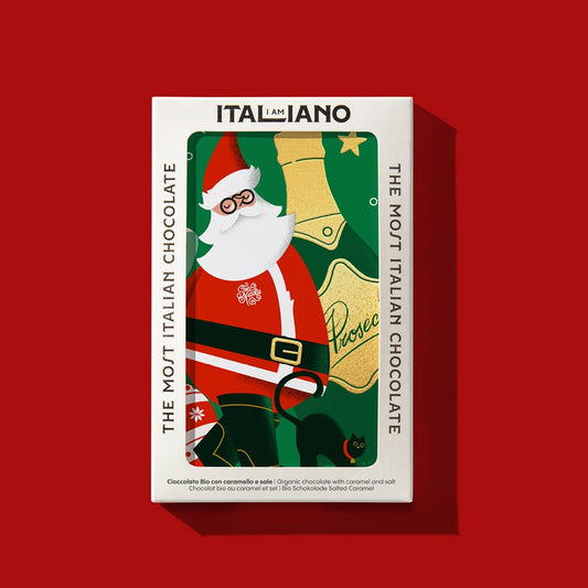 Eine festliche Schachtel I AM ITALIANO Prosecco Bio-Schokolade mit Karamell und Salz zeigt den Weihnachtsmann mit einer Glocke auf grünem Hintergrund. Die Verpackung trägt die Aufschrift "The Most Italian Chocolate" und ist mit weihnachtlichen Motiven dekoriert.