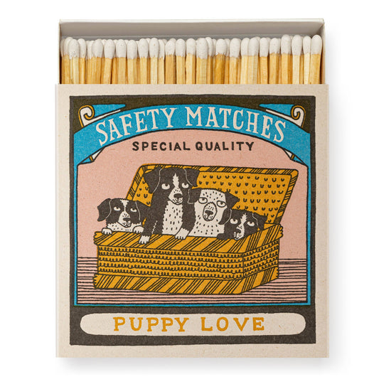 Die quadratischen Streichholzschachteln "Puppy Love" von Archivist Gallery zeigen Charlotte Farmers Design von drei Welpen in einem Korb. Auf der Schachtel stehen SAFETY MATCHES SPECIAL QUALITY und PUPPY LOVE, mit weißen Streichholzköpfen.