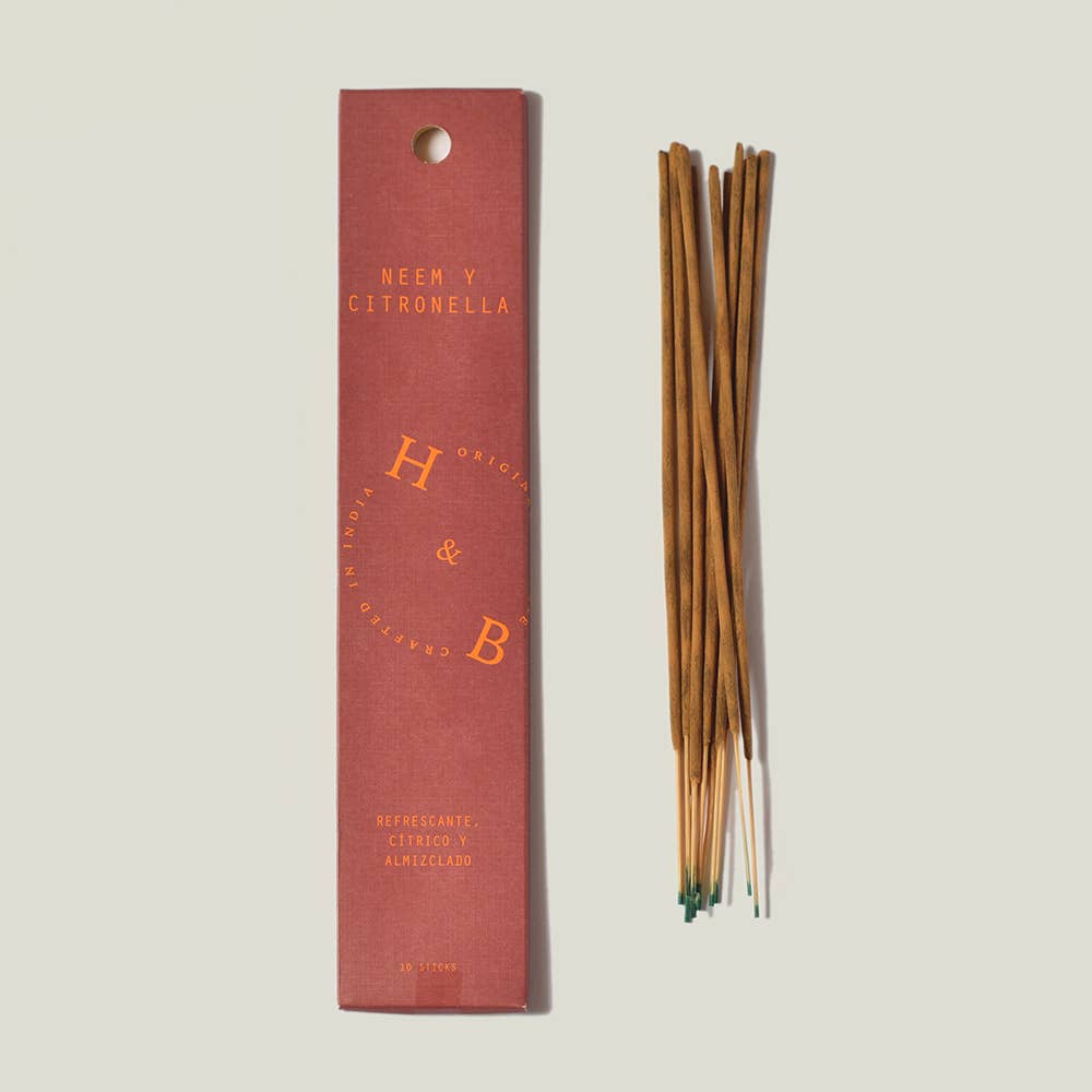 Eine rosafarbene rechteckige H&B-Weihrauchdose mit der Aufschrift "Neem- und Citronella-Weihrauch (gegen Mücken)" liegt neben einem Bündel brauner Räucherstäbchen mit grünen Spitzen, die ordentlich auf einem hellen Hintergrund angeordnet sind.