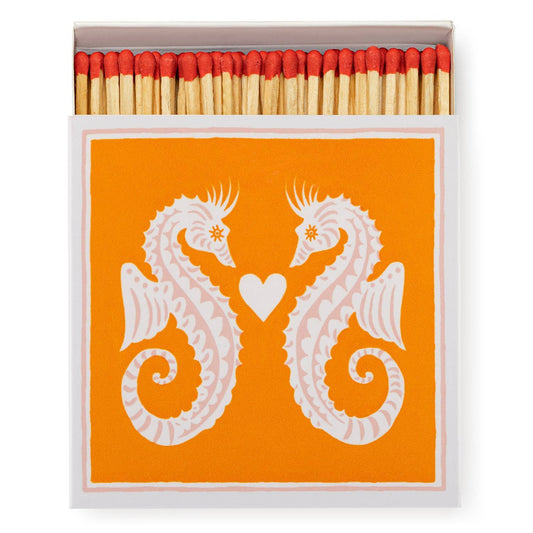 Eine geöffnete Schachtel Archivist Gallery - Seahorses | Square - Safety Matches zeigt einen orangefarbenen Deckel mit zwei weißen Seepferdchen, die sich gegenüberstehen und ein kleines Herz dazwischen - ein entzückendes Archivist Gallery-Design.