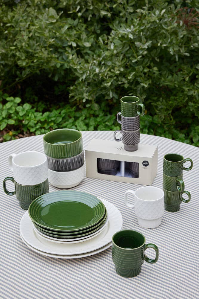 Ein Set aus grüner, weißer und grauer Sagaform GmbH Coffee & More Teetasse, 2-tlg. ist auf einer gestreiften Tischdecke im Freien mit Grünzeug im Hintergrund angeordnet. Einige Tassen sind gestapelt und ein verpacktes Set ist ausgestellt.