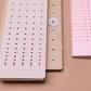 Ein Bleistift und drei Tinne Mia - Aufgabenliste - Mellow Rose Notizblöcke von Tinne Mia, hergestellt aus FSC®-zertifiziertem Papier, in Rosa und Beige mit perforierten Deckeln mit kreisförmigen Löchern, angeordnet auf einer hellbraunen Oberfläche.
