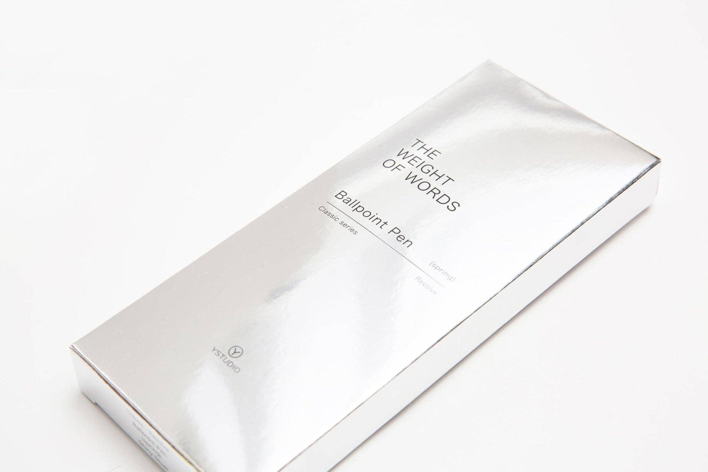 Auf einer weißen Fläche ist eine glatte, reflektierende, metallisch silberne Schachtel mit der Aufschrift ENTREPÔT - YSTUDIO - Klassischer Drehkugelschreiber Feder (Glänzendes Silber) zu sehen. Die Verpackung sieht minimalistisch und elegant aus.