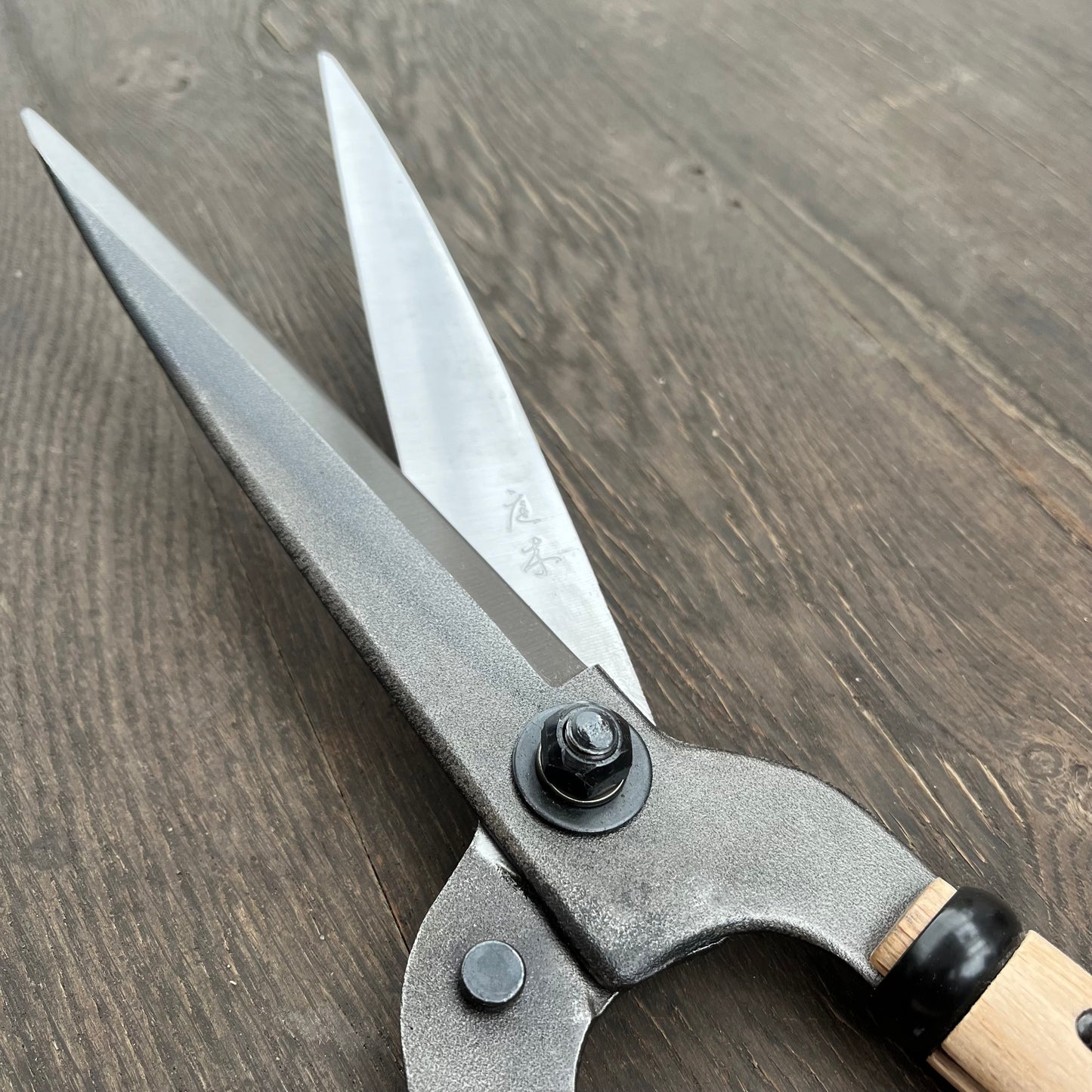 Eine Nahaufnahme der Niwaki FSC Heckenschere von Niwaki mit scharfen silbernen Klingen und einem Holzgriff aus FSC-zertifiziertem Holz, der auf einer dunklen Holzoberfläche ruht.